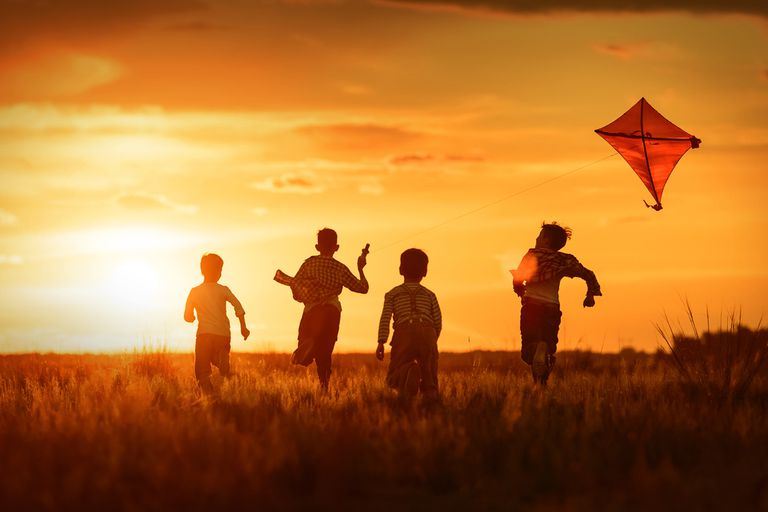  Four children running in a field flying a kite at sunset.